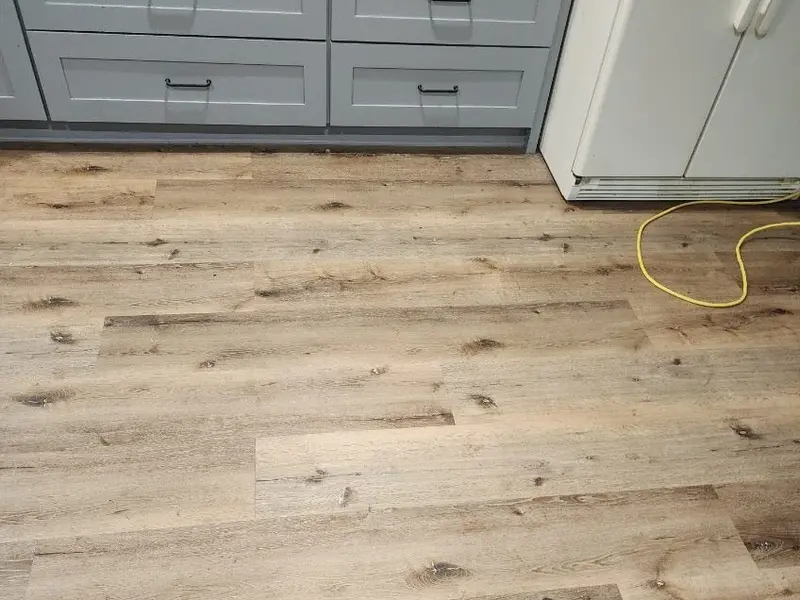 Photo of the same wood-look plank kitchen floor after cleaning, beside gray drawers and a refrigerator.